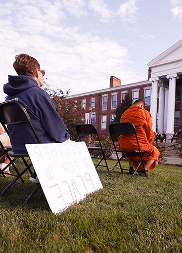 A woman sits on the lawn of Boyden Hall with a sign that says "Together for Peace"